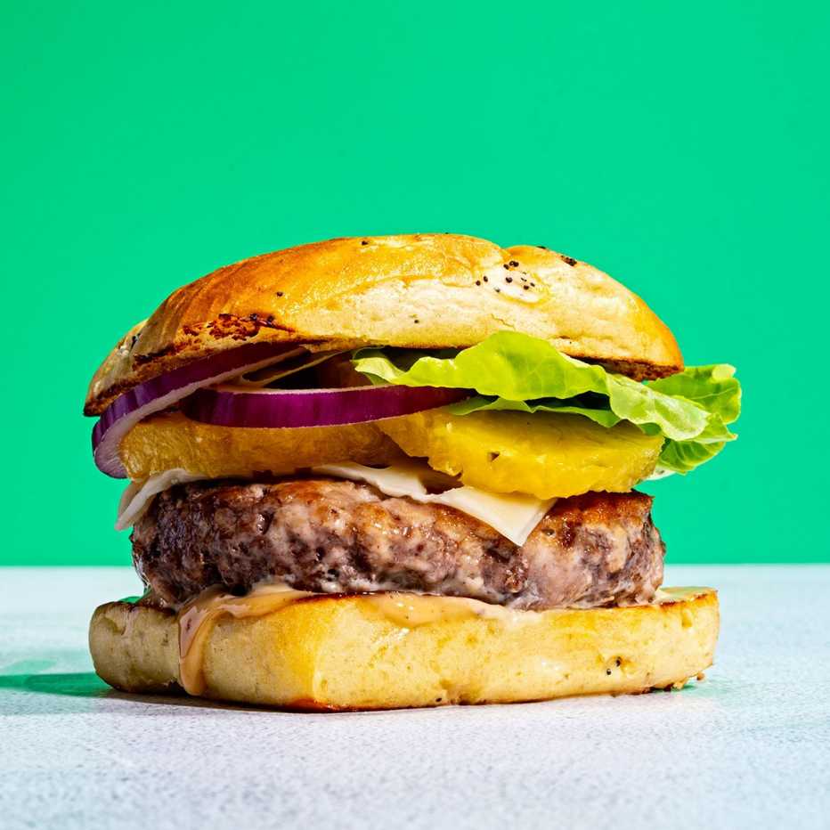 Una hamburguesa con piña, cebolla, lechuga y salsa.