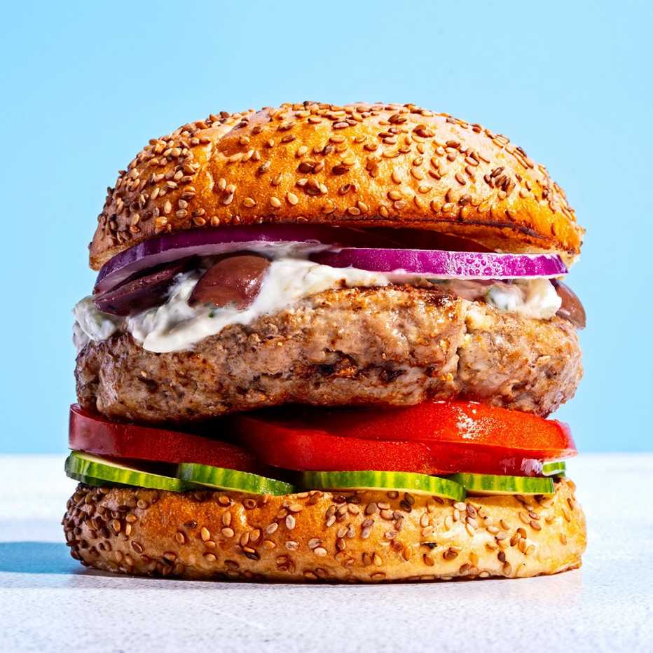 Una hamburguesa con pepino, tomate, cebolla roja y salsa.