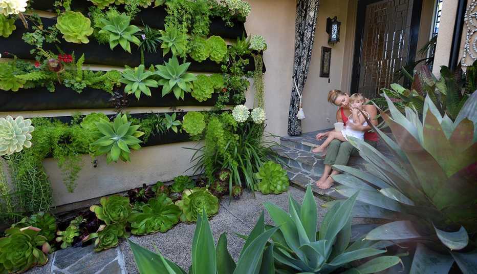 Mujer con una niña pequeña afuera de su casa en frente de un jardín vertical Mujer con una niña pequeña afuera de su casa en frente de un jardín vertical