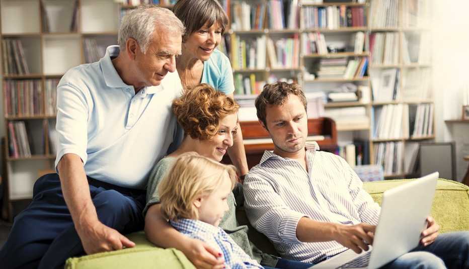 Familia sentada en un sillón viendo algo en una computadora portátil