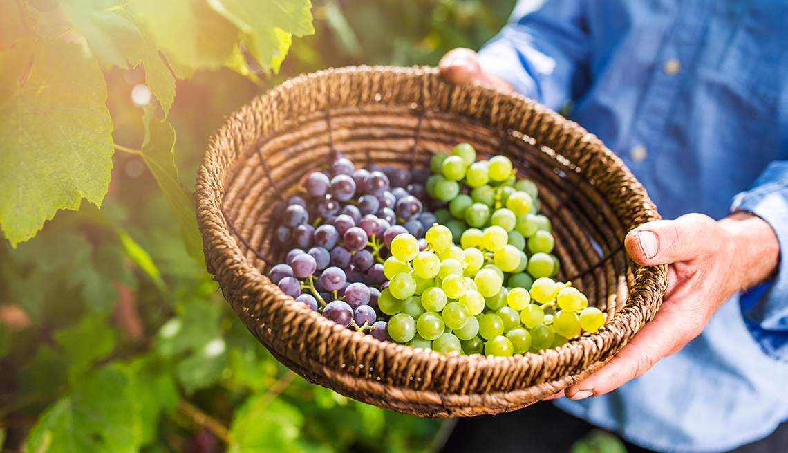 Manos sosteniendo una canasta con uvas verdes y moradas
