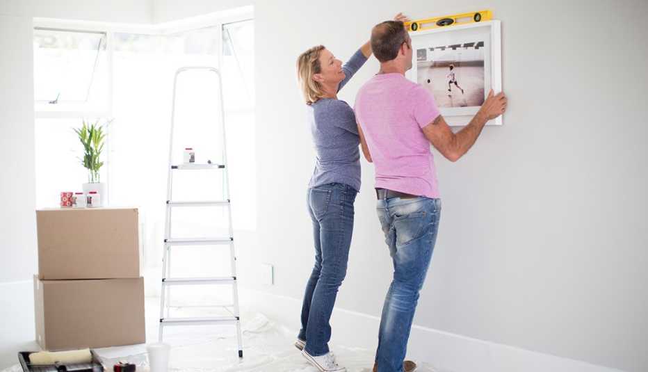 Pareja cuelga un cuadro en una pared de su casa.