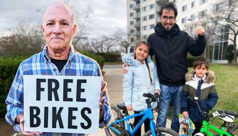 ‘Bike Man’ Repairs, Gives Away Nearly 600 Free Bicycles a man holds a sign that says free bikes while a family stands behind him with blue and green bikes