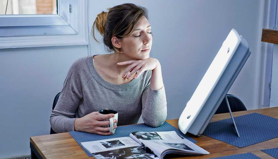 Mujer tomando café mientras está en una sesión de fototerapia