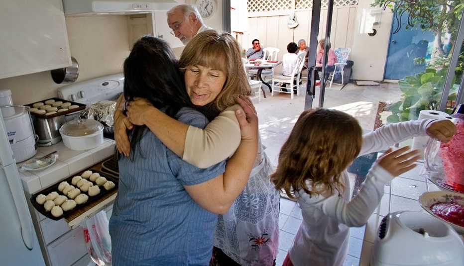 Una mujer da la bienvenida a un familiar en su cocina mientras prepara la cena