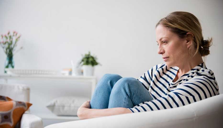 Una mujer sentada en un sillón luciendo triste.