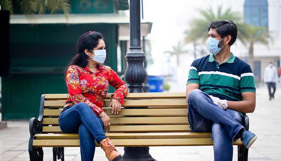 Una mujer y un hombre con máscaras sentados en una silla del parque