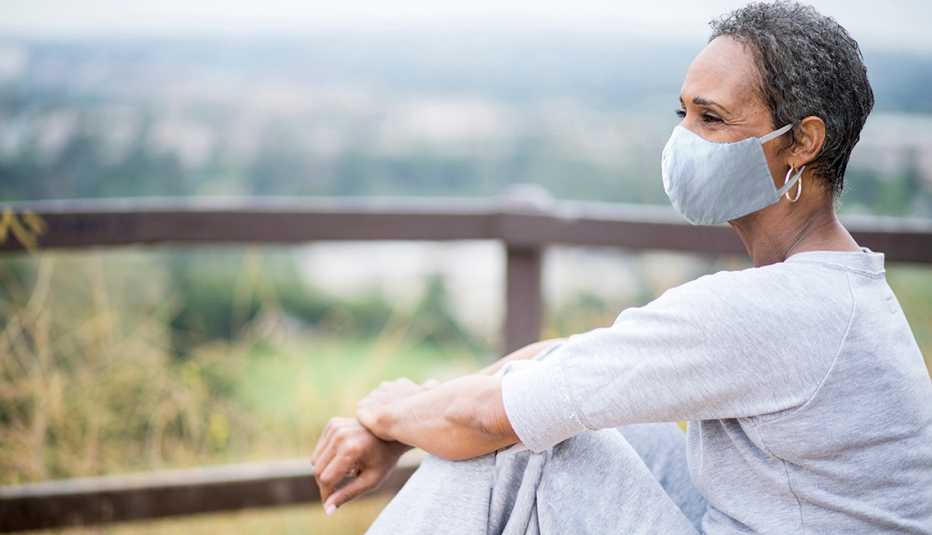 Una mujer sentada en exteriores lleva puesta una máscara Una mujer sentada en exteriores lleva puesta una máscara