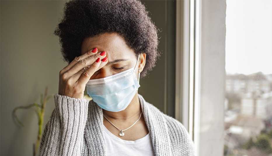 Mujer se toca la frente mientras lleva puesta una mascarilla quirúrgica Mujer se toca la frente mientras lleva puesta una mascarilla quirúrgica