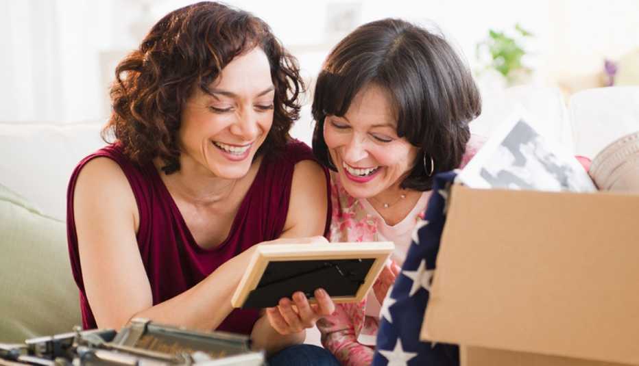 Dos mujeres mayores observan un portaretrato y sonríen.