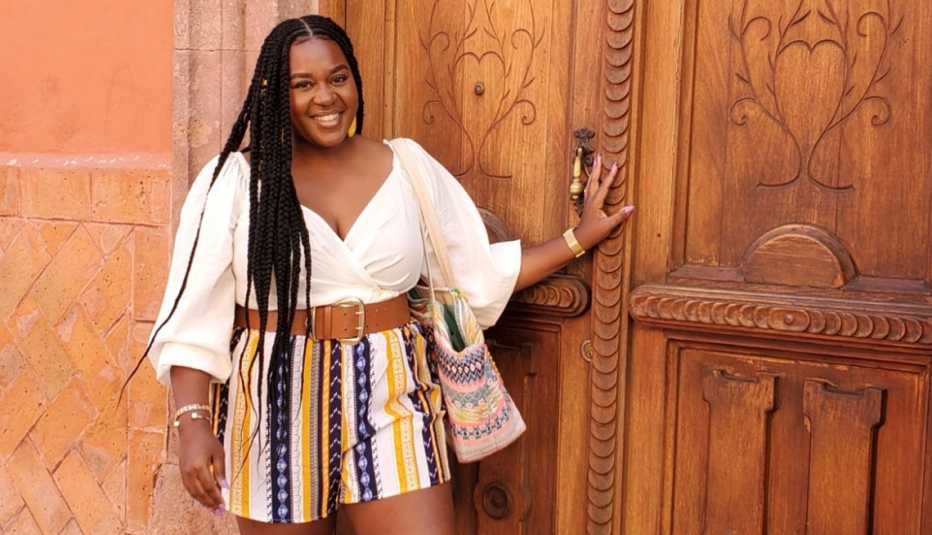 La ganadora de Benefits Badass, de AARP, Jihane Jeanty, de pie frente a una puerta de madera. La ganadora de Benefits Badass, de AARP, Jihane Jeanty, de pie frente a una puerta de madera.