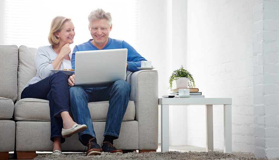 Pareja mayor sentada en sofa, sonriendo enfrente se un computador portátil