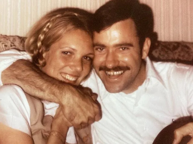 una vieja foto muestra a Suzy y Bill Bailey, vestidos de blanco, agarrados de mano y sonriendo sentados en un sofá 