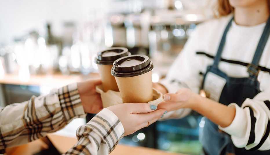 una barista entrega dos tazas de café para llevar a un cliente