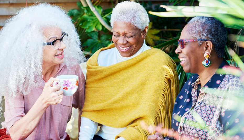Tres mujeres conversando y riendo mientras toman té en un jardín