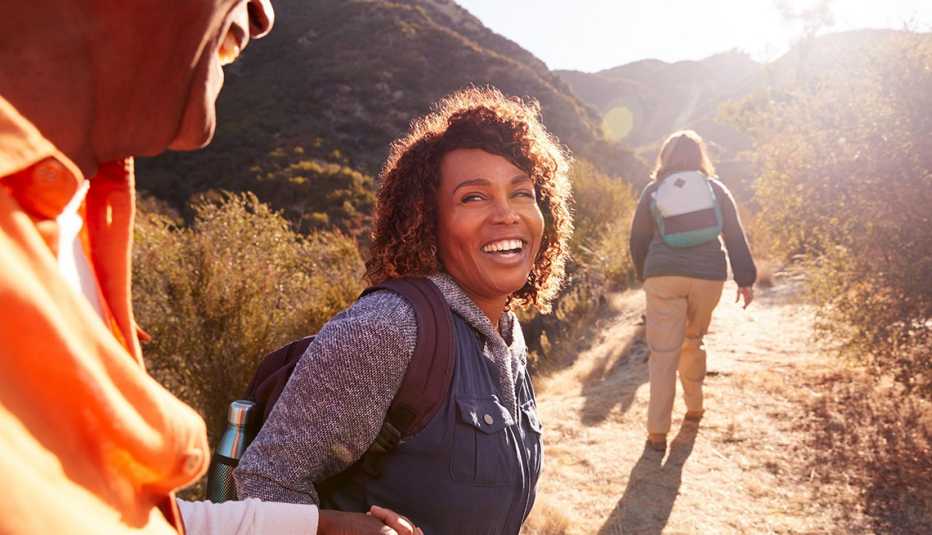 una mujer en un viaje de senderismo sostiene la mano de un hombre mientras otra excursionista camina por un sendero del suroeste durante el día