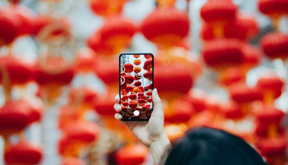Mujer sostiene un teléfono para tomar una foto de faroles de papel rojos