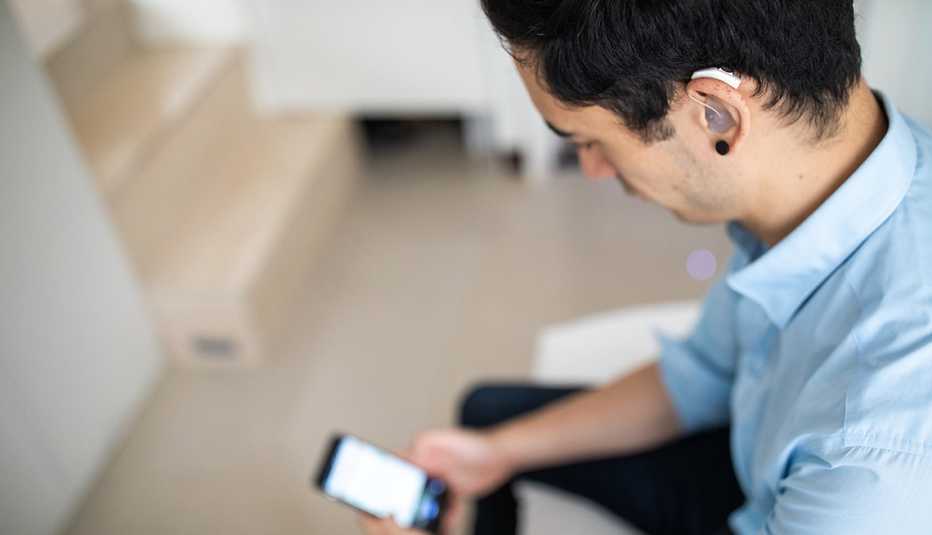 Un hombre con audífono en el oído mira su teléfono Un hombre con audífono en el oído mira su teléfono