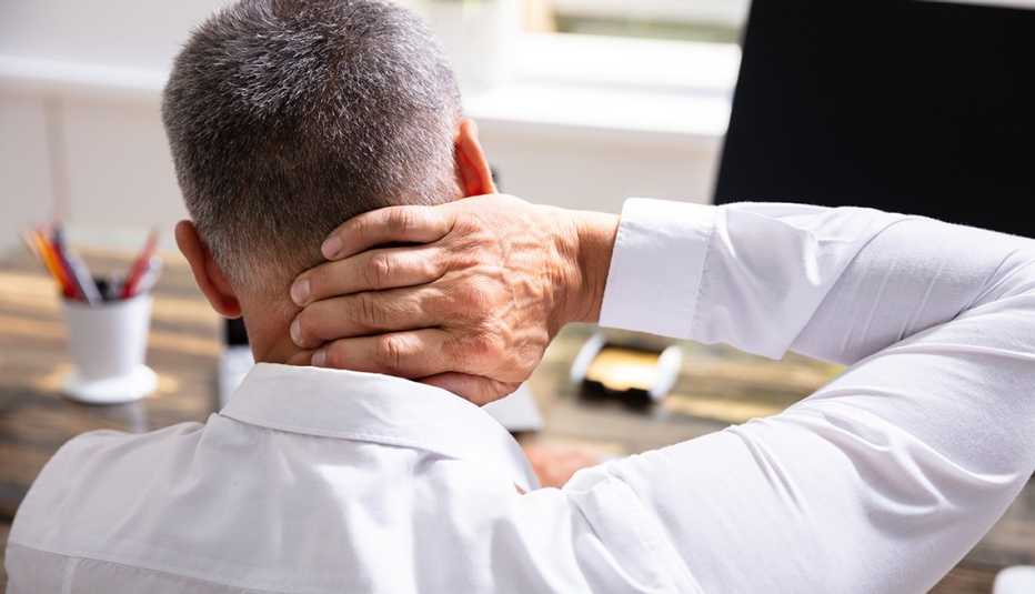 Hombre con la mano en el cuello dolorido frente a su computadora Hombre con la mano en el cuello dolorido frente a su computadora