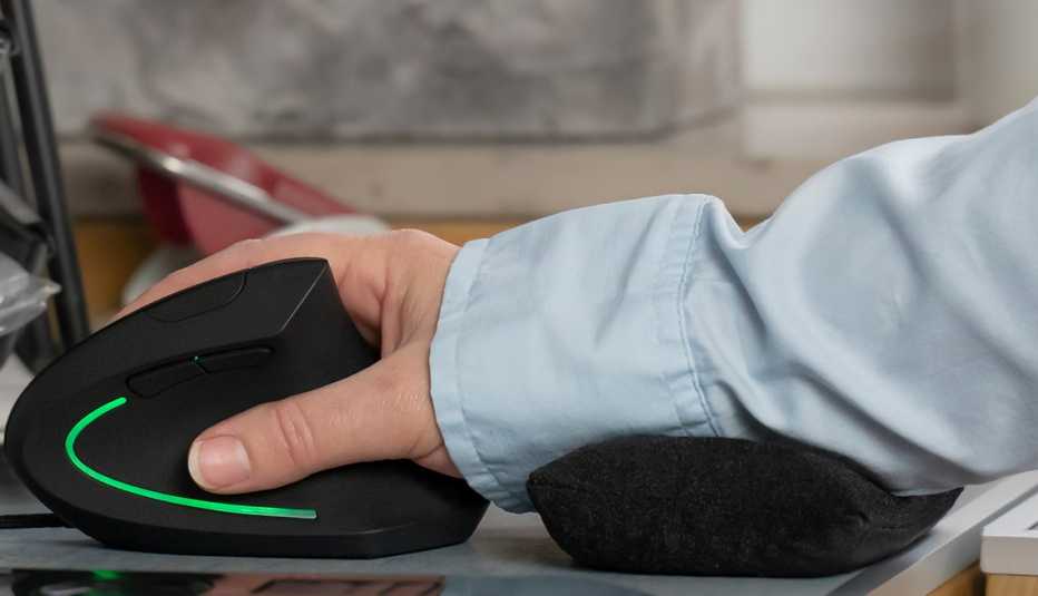 Mano en un escritorio descansa sobre un ratón ergonómico de computadora