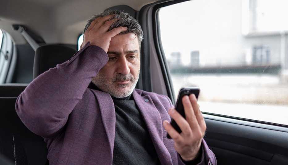 Un hombre que mira su teléfono se toma la cabeza