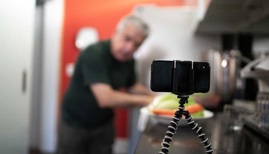 Hombre que está fuera de foco mira hacia un teléfono inteligente que funciona como su cámara web Hombre que está fuera de foco mira hacia un teléfono inteligente que funciona como su cámara web