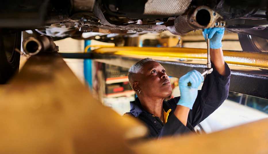 una mecánica mira la parte inferior de un auto