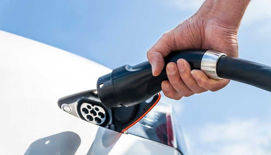 Hombre sostiene un cargador eléctrico mientras se prepara para cargar su vehículo Hombre sostiene un cargador eléctrico mientras se prepara para cargar su vehículo