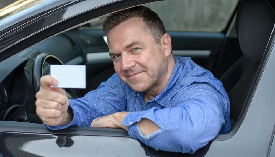 un hombre muestra su licencia de conducir un hombre sonriendo sostiene su licencia de conducir desde el asiento de su auto