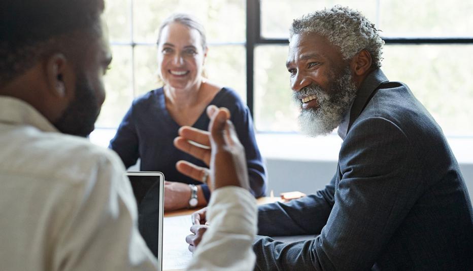 Does Saving for Emergencies Improve Productivity at Work? Smiling businessman looking at male coworker while sitting in board room during office meeting