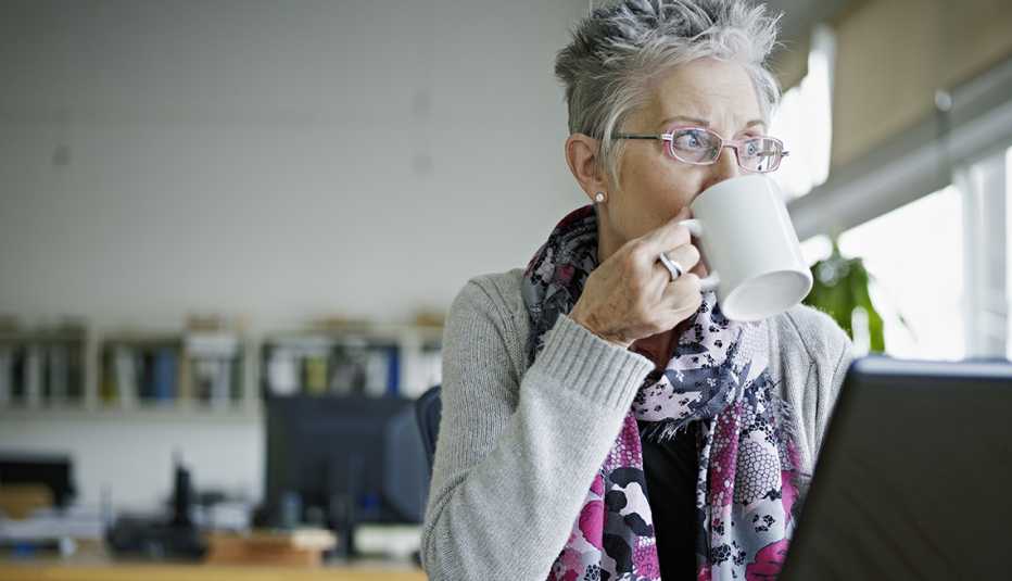 Ejecutiva en su oficina sentada frente a su computadora mientras toma café y mira por la ventana. Ejecutiva en su oficina sentada frente a su computadora mientras toma café y mira por la ventana.