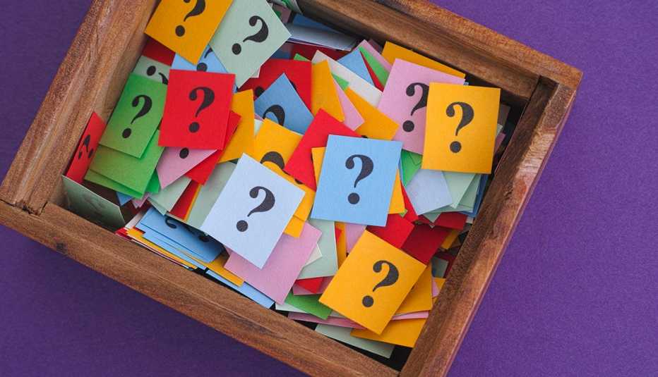 Caja de madera llena con papeles de colores que tienen un signo de interrogación