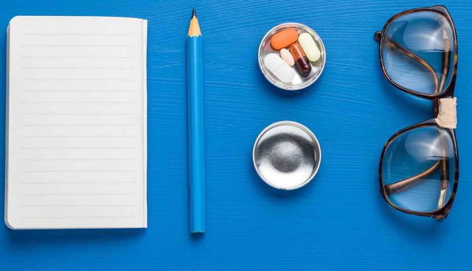 Libreta, lápiz, píldoras y espejuelos sobre un fondo azul Libreta, lápiz, píldoras y espejuelos sobre un fondo azul