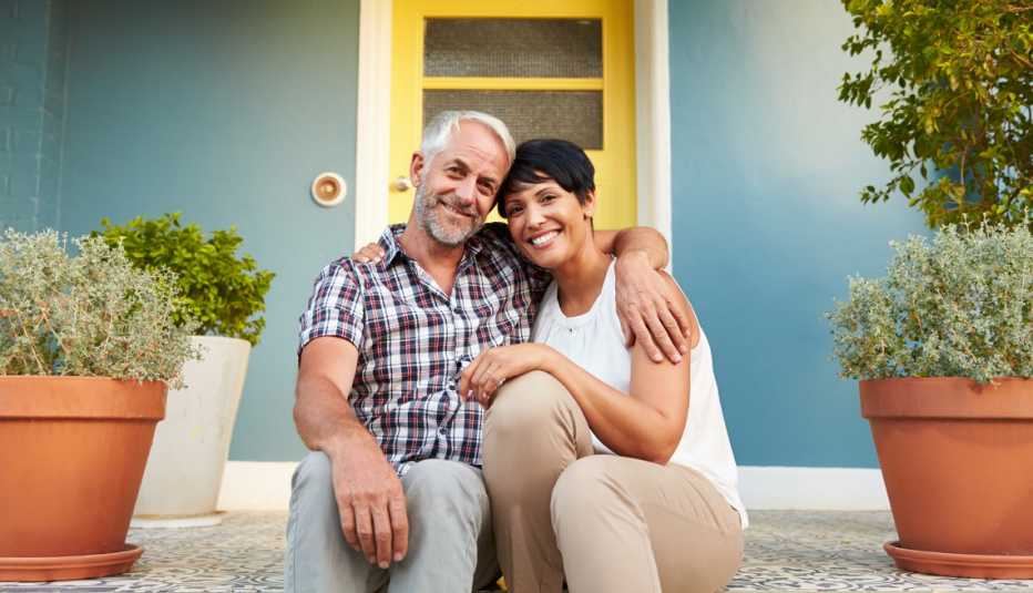Pareja en edad madura sentada frente a la entrada de una casa.