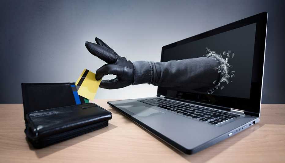 Mano saliendo del computador y sacando una tarjeta de crédito de una billetera