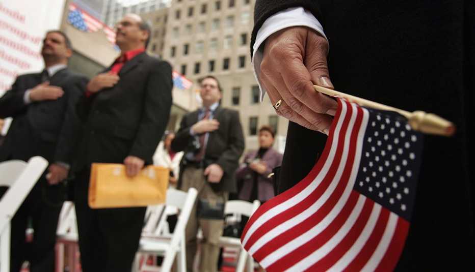 Mano sosteniendo una bandera americana con personas detrás jurando como ciudadanos Mano sosteniendo una bandera americana con personas detrás jurando como ciudadanos