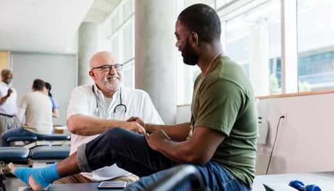 Un hombre sentado en una cama siendo atendido por un médico Un hombre sentado en una cama siendo atendido por un médico