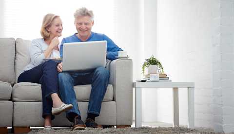 Pareja mayor sentada en sofa, sonriendo enfrente se un computador portátil Pareja mayor sentada en sofa, sonriendo enfrente se un computador portátil