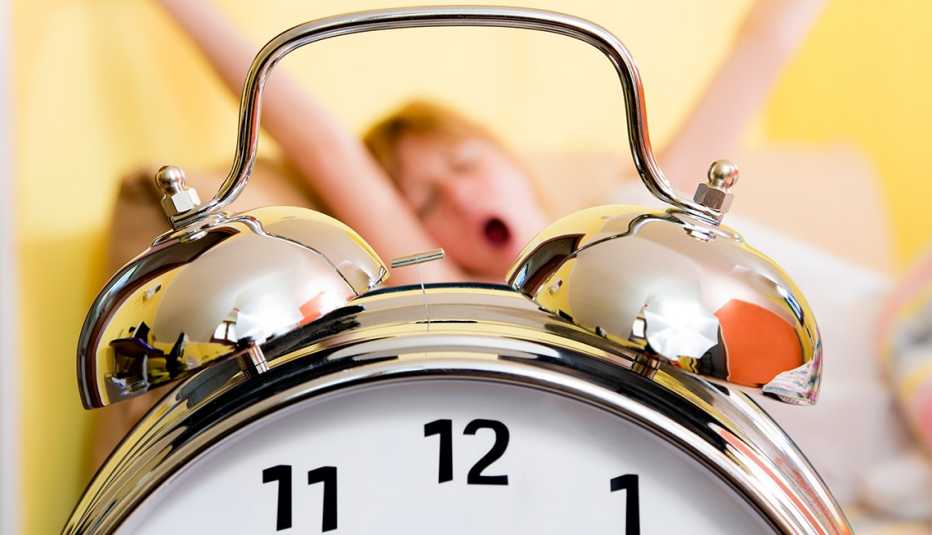 Reloj en primer plano y mujer bostezando al fondo