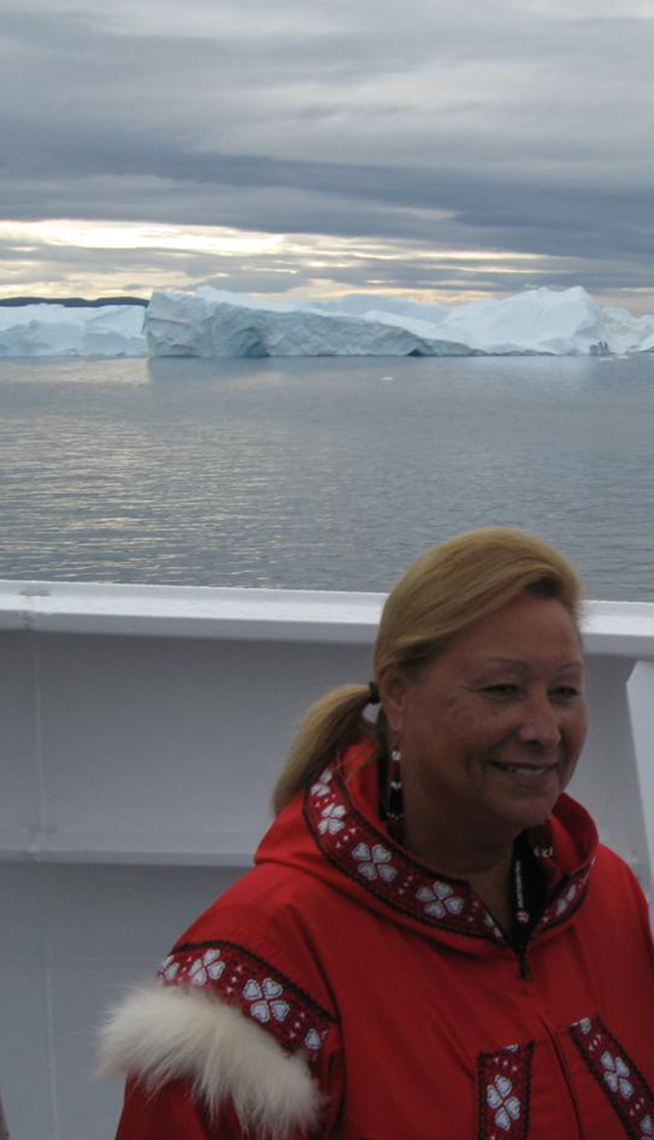 Pat Cochran, con un abrigo tradicional nativo de Alaska, parada en un bote frente a un glaciar.