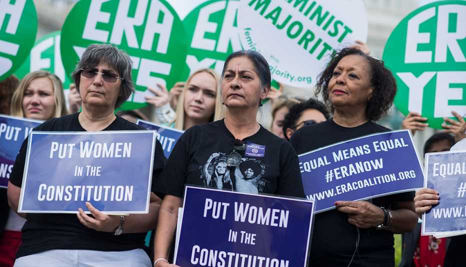 Grupo de mujeres sostienen carteles que dicen en inglés -E R A Yes- y -Put Women in the Constitution- Grupo de mujeres sostienen carteles que dicen en inglés -E R A Yes- y -Put Women in the Constitution-