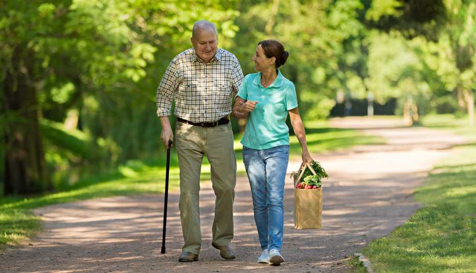  Adulto mayor y cuidador caminan al aire libre.