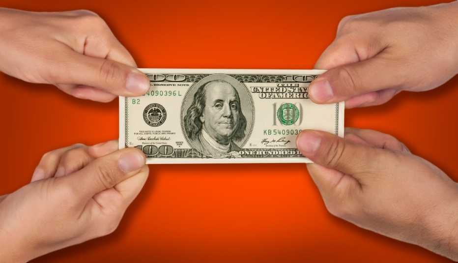 Manos de un hombre y una mujer estirando un billete de 100 dólares