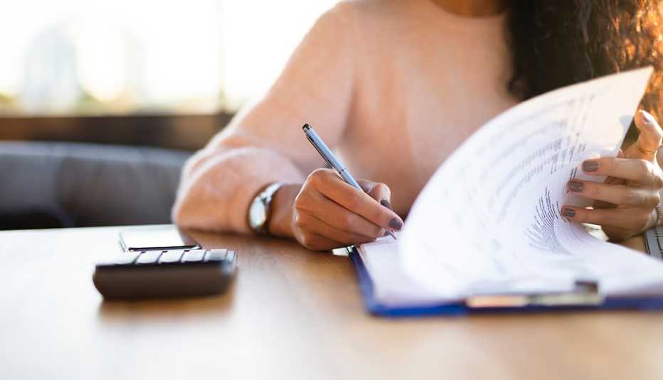 Una mujer llenando un formulario con una calculadora.