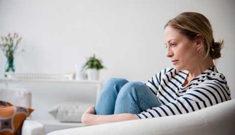 Una mujer sentada en un sillón luciendo triste.