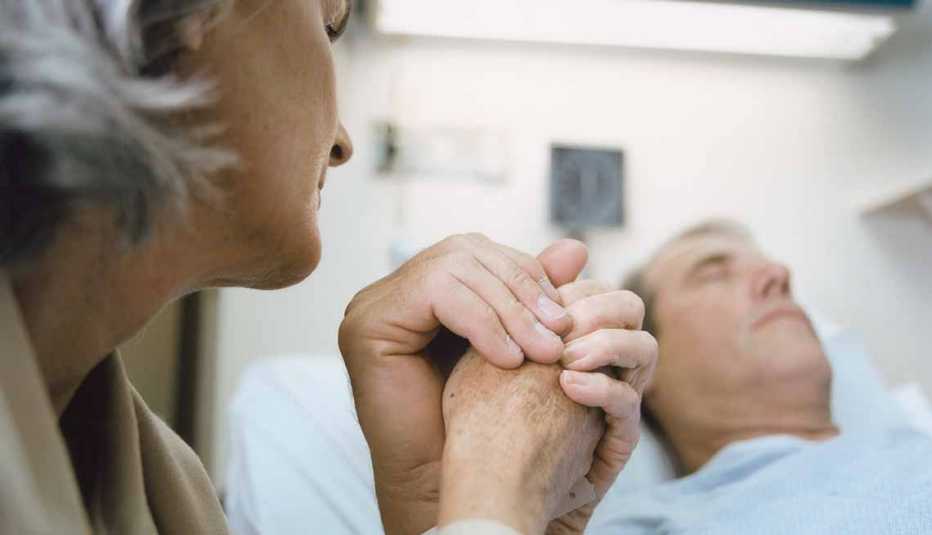 Mujer sostiene la mano de un hombre que está en el hospital - La alimentación artificial al final de la vida Mujer sostiene la mano de un hombre que está en el hospital - La alimentación artificial al final de la vida