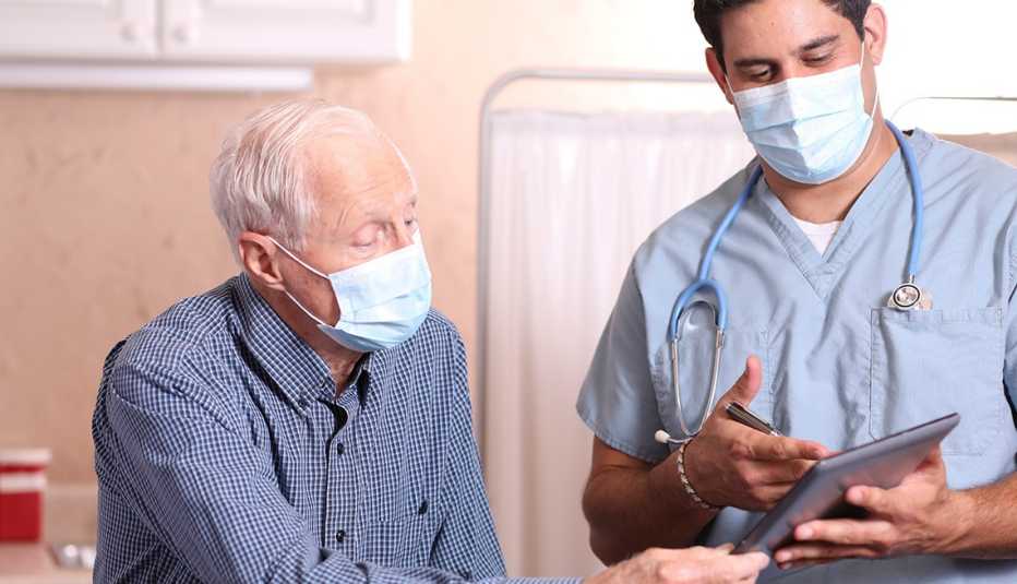 Un hombre conversa con su doctor, ambos usan mascarilla
