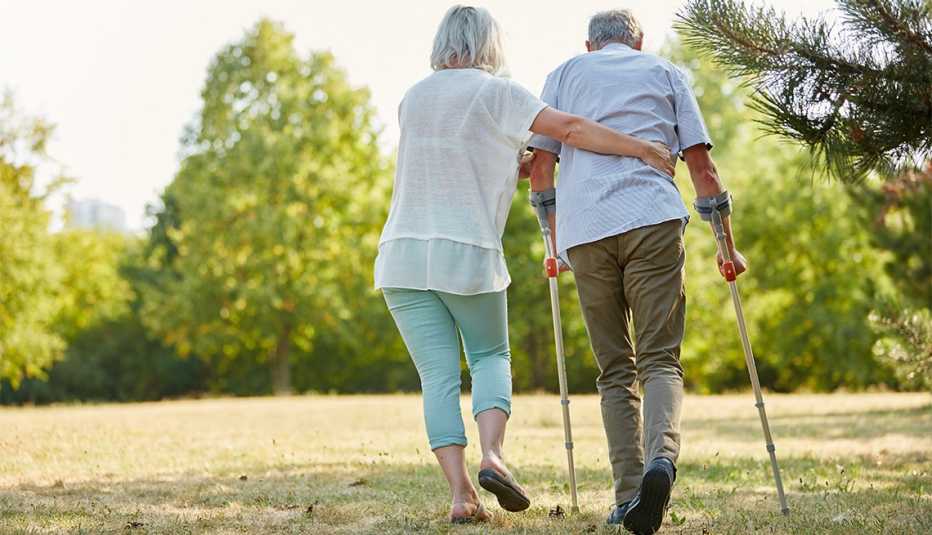 Cuidador ayuda a un hombre a caminar con muletas en un parque. Cuidador ayuda a un hombre a caminar con muletas en un parque.