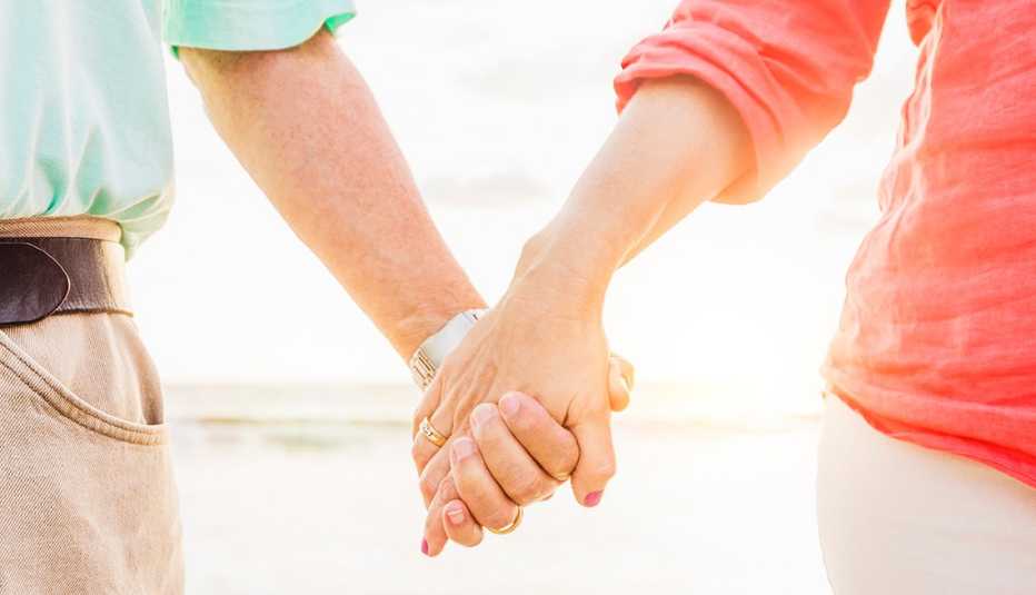 Pareja agarrada de la mano mientras camina por la playa.