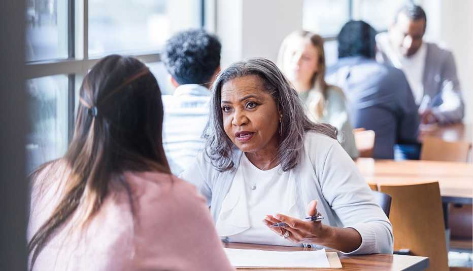 Una consejera conversa con otra mujer, al fondo se ven otros consejeros